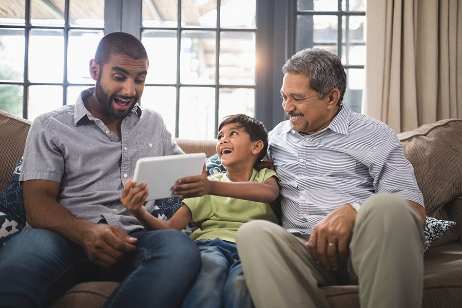 Blog - Portrait of a Cheerful Father and Grandfather Having Fun Sitting on the Sofa Watching a Young Boy Play on a Tablet