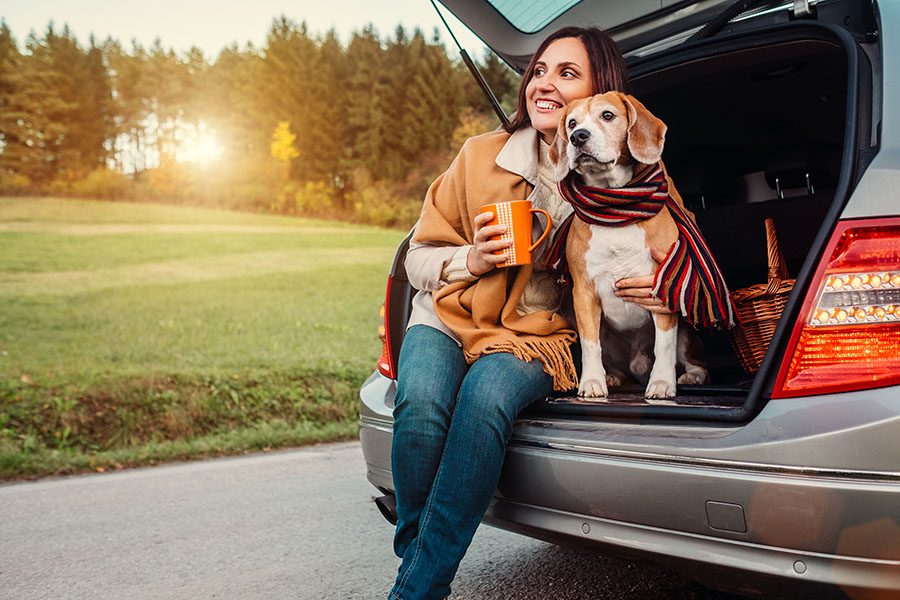 Contact - Portrait of a Smiling Woman Sitting with Her Dog in the Back Trunk of Her SUV on a Country Road Enjoying the View of the Sunset on a Nice Fall Day
